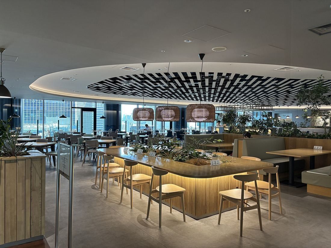 Daikin: Dining area with wooden tables and stools under a circular slatted ceiling feature, windows behind