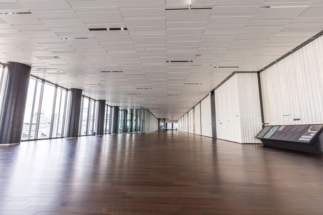 Daikin: Long, empty lobby with a dark wood floor, round columns along the windows and pale wall panels