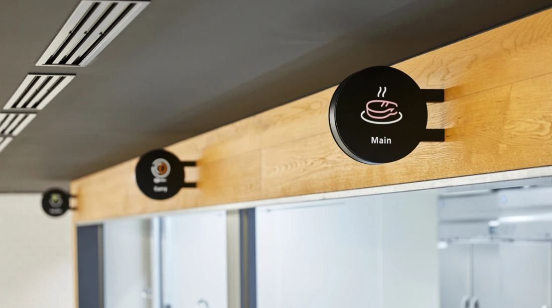 Daikin: Round black room signs with simple pictograms mounted on a wood-clad wall above glass partitions