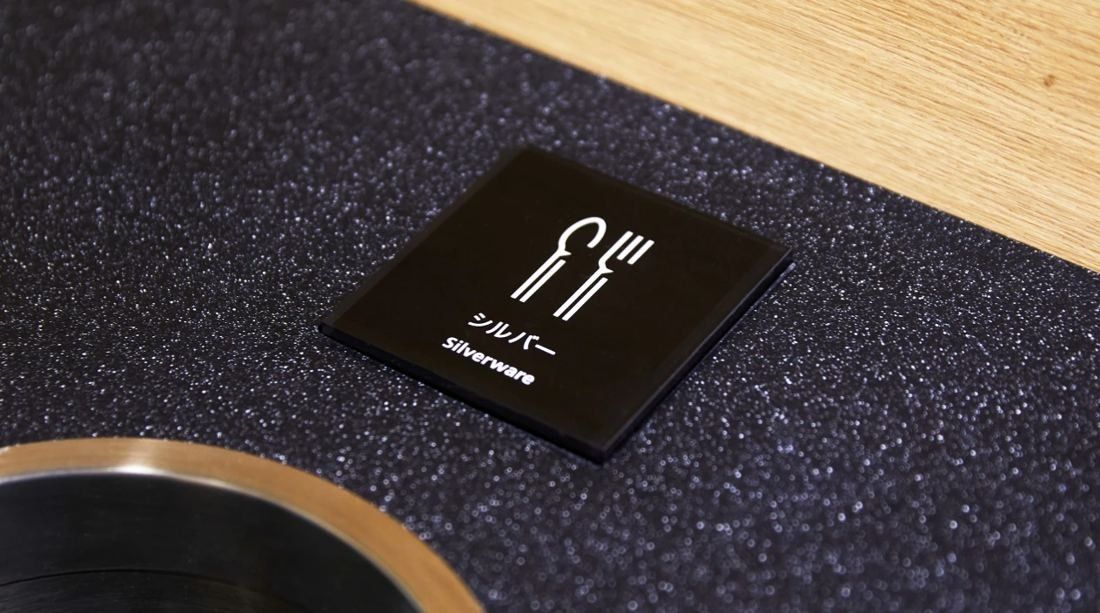 Daikin: Small black square sign with a fork-and-knife pictogram on a dark speckled surface
