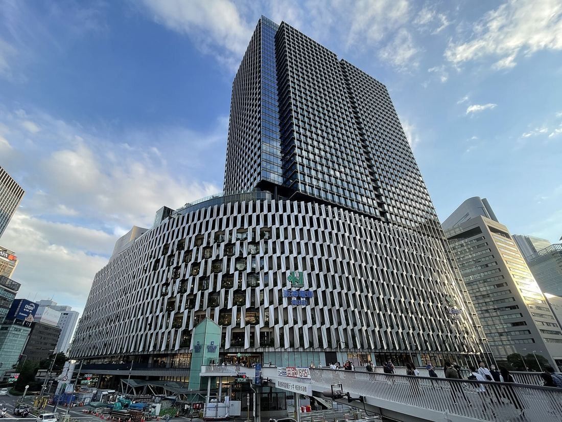 Daikin: The tower and its curved, louvered lower block seen from a pedestrian deck under a cloudy sky