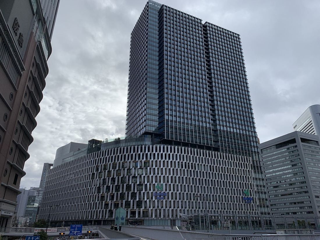 Daikin: The tower and its low curved base seen from a wide street under a grey sky