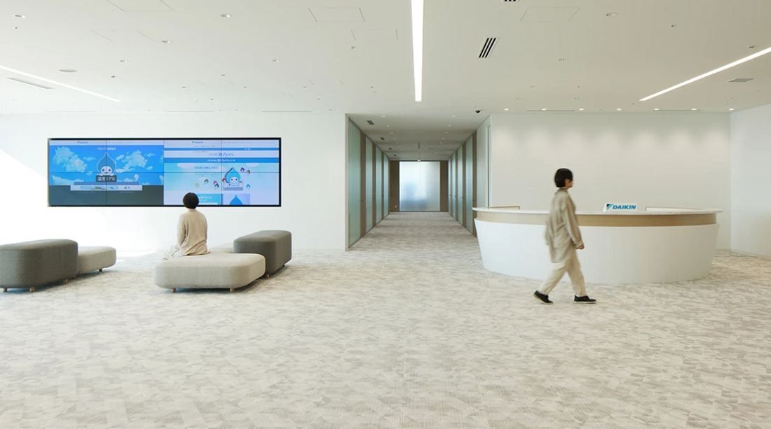 Daikin: White reception area with a curved counter, low upholstered benches and a wide video wall