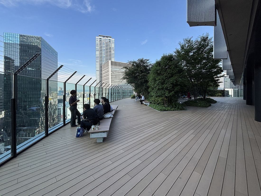 Daikin: Wooden roof terrace with railings, benches and trees, with high-rises beyond