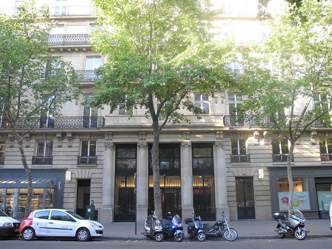 Haussmann-era stone building behind street trees, with parked scooters and a car