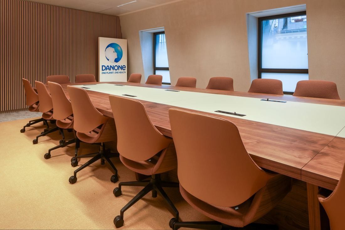 Danone: Long wooden boardroom table with rows of terracotta swivel chairs and a Danone banner