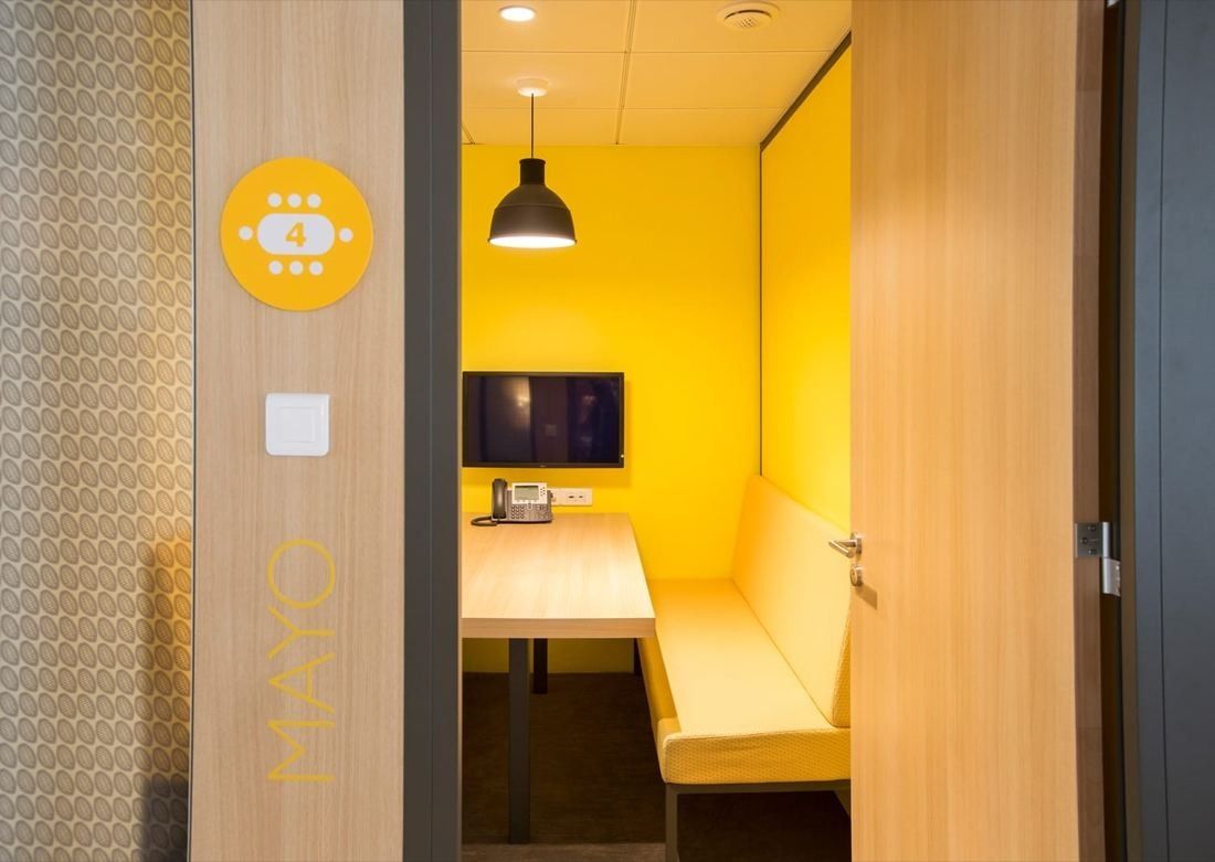 Danone: Small yellow meeting room with a bench, table and screen behind a wooden door
