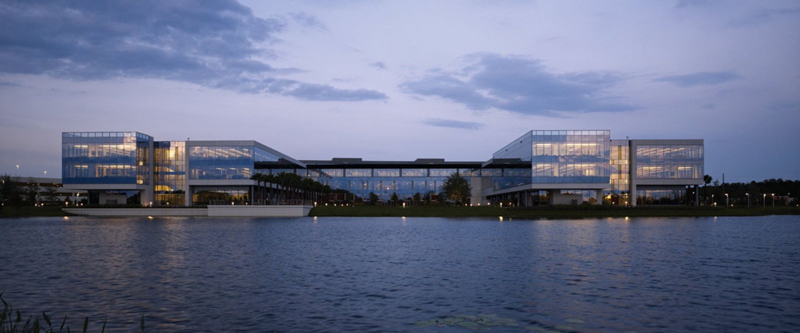A long low glass headquarters lit at dusk across a wide lake
