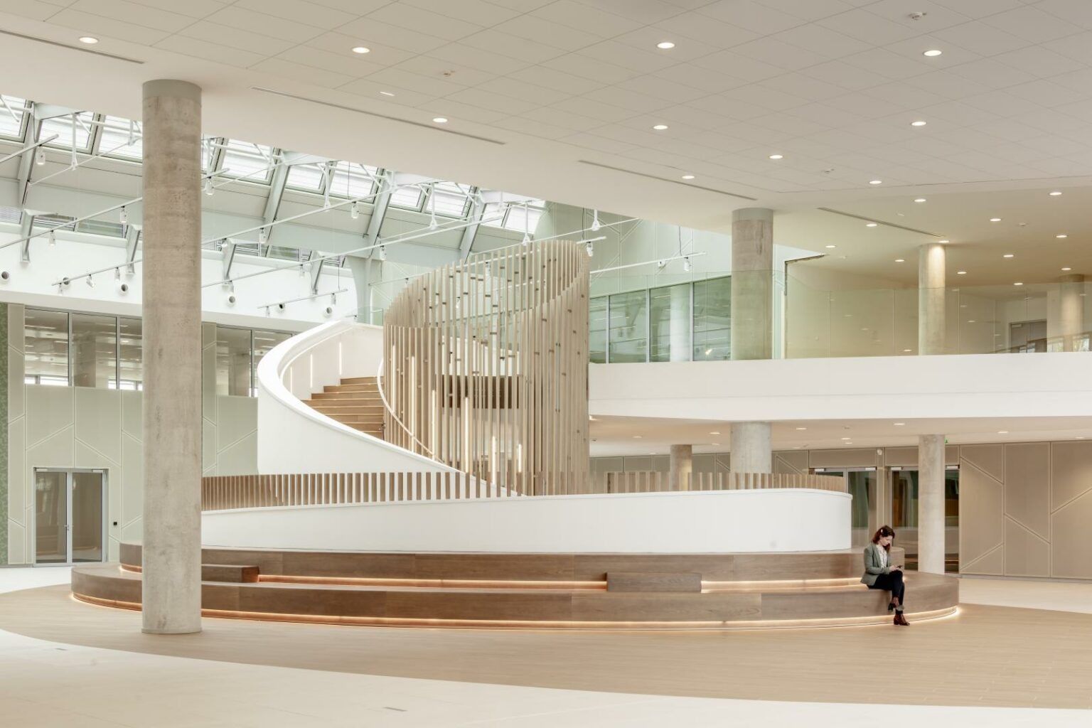 Dassault Systèmes: Bright hall with a curving white balustrade and timber screen