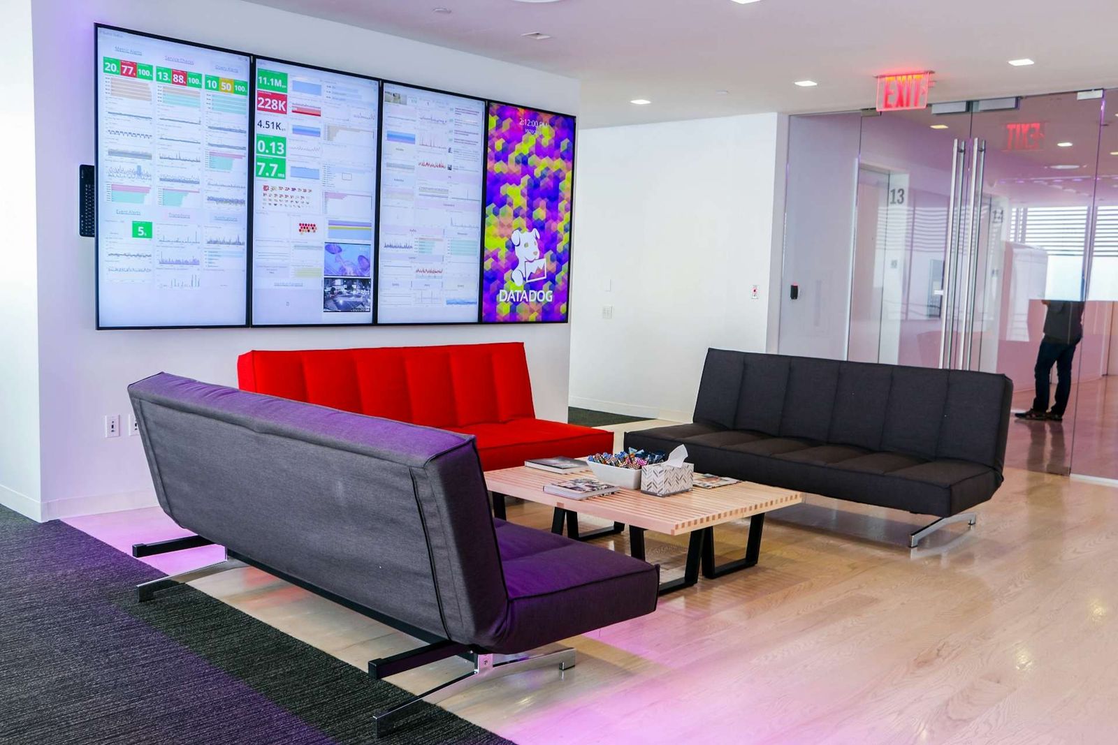 Datadog: Lounge with red and black sofas under a wall of dashboard screens