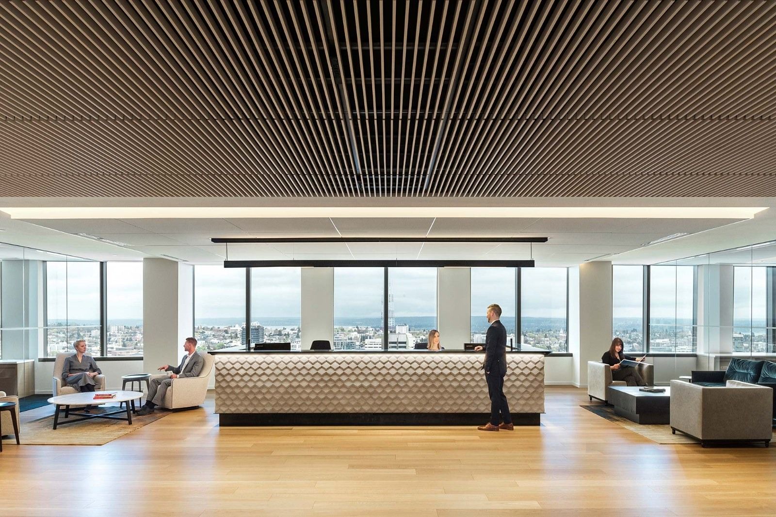 A long reception desk under a wooden slat ceiling with city views