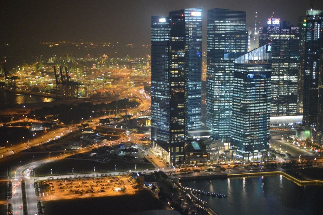 Aerial night view of the Marina Bay Financial Centre towers lit up, with the port lights beyond