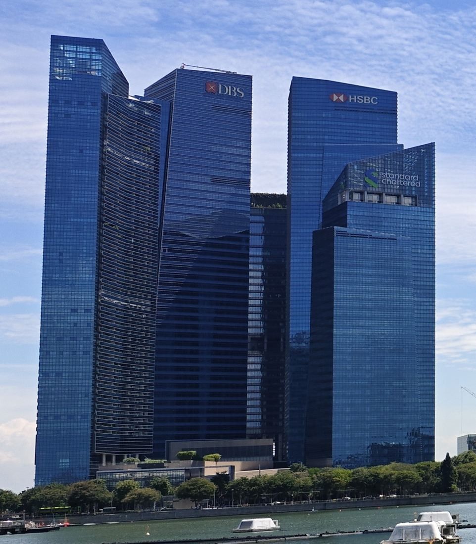 DBS Bank: Blue glass towers of Marina Bay Financial Centre seen from the waterfront, DBS logos at the top