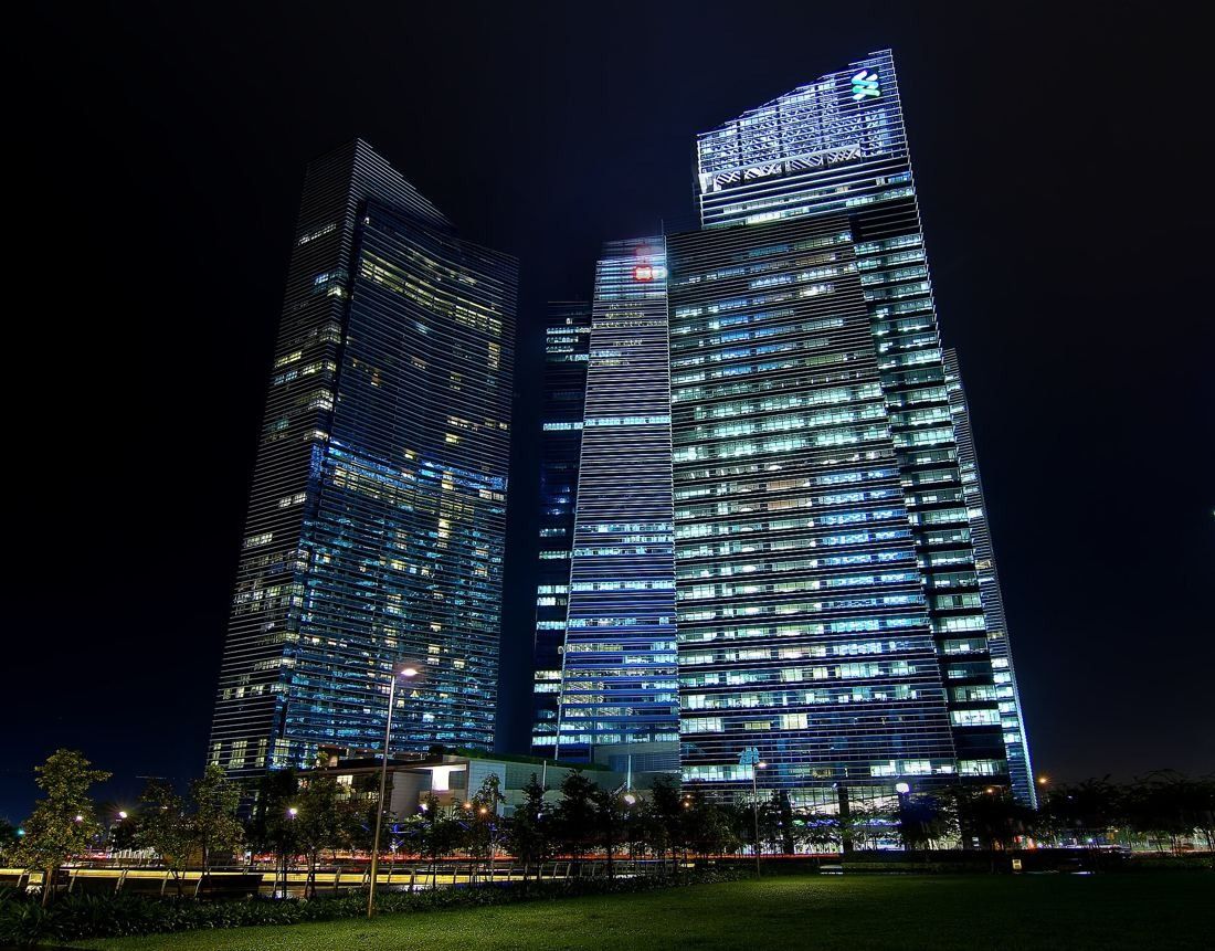 DBS Bank: Glass towers lit at night seen from a dark lawn
