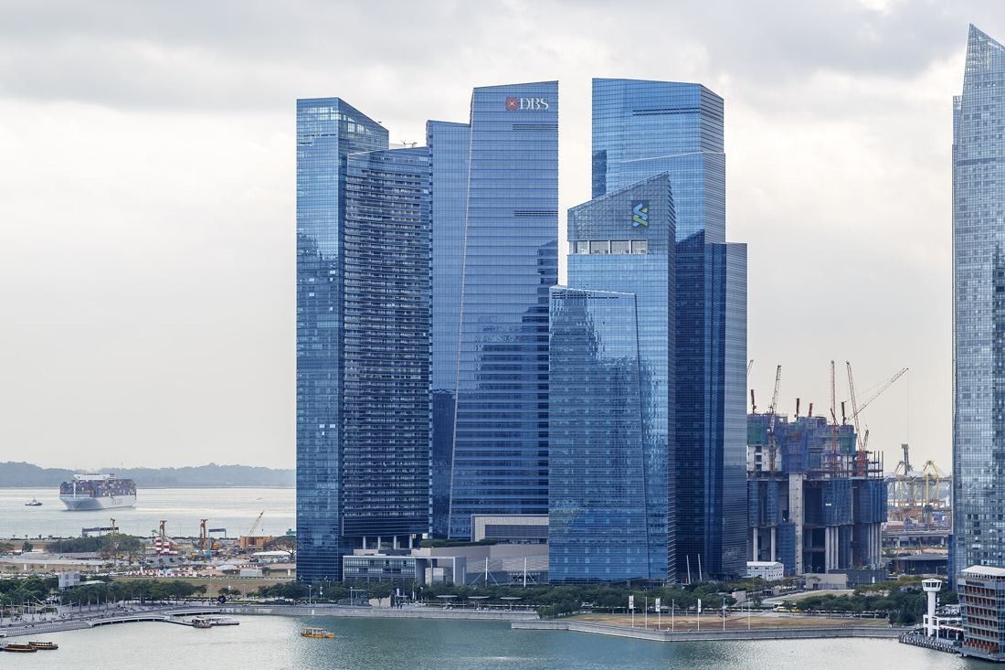 DBS Bank: Glass towers of Marina Bay Financial Centre rising over the bay, with a DBS logo near the top of one tower