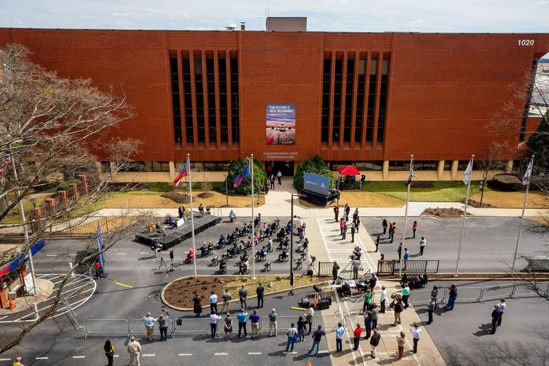 Delta Air Lines: Aerial view of a long red-brick office building with flagpoles and a plaza where chairs and a small stage are set up