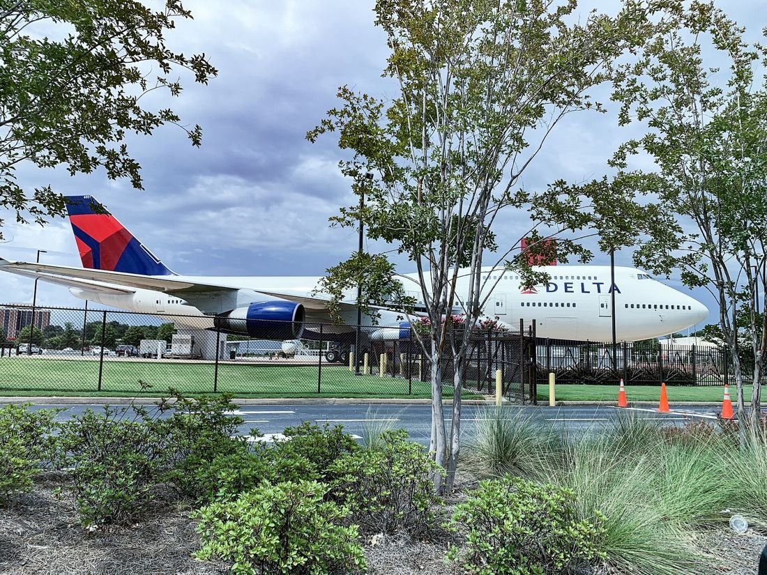 Delta Air Lines: Boeing 747 in Delta livery seen through trees and landscaped grasses beside a road