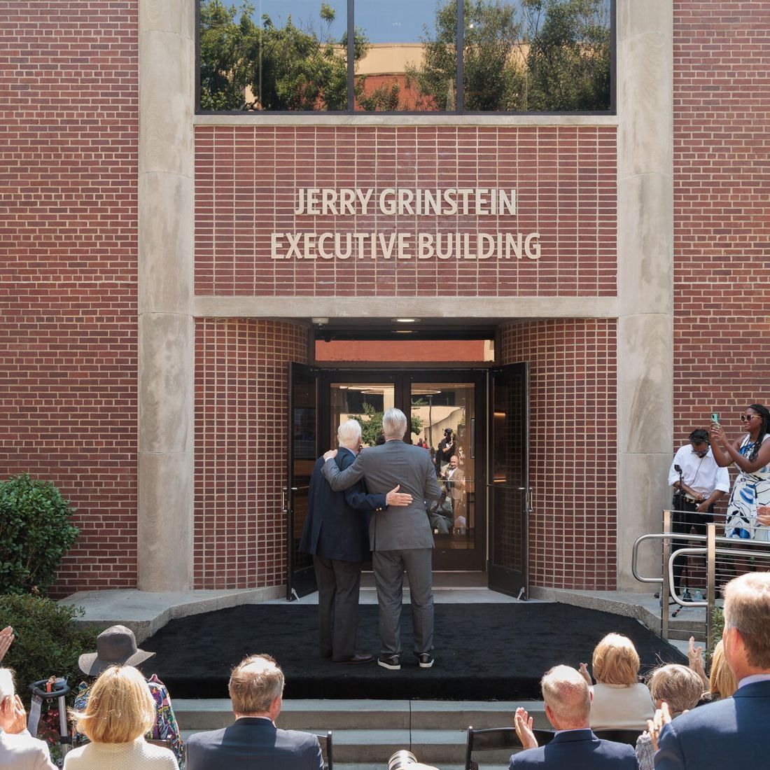 Delta Air Lines: Brick entrance under lettering reading Jerry Grinstein Executive Building, seen over the heads of a seated audience