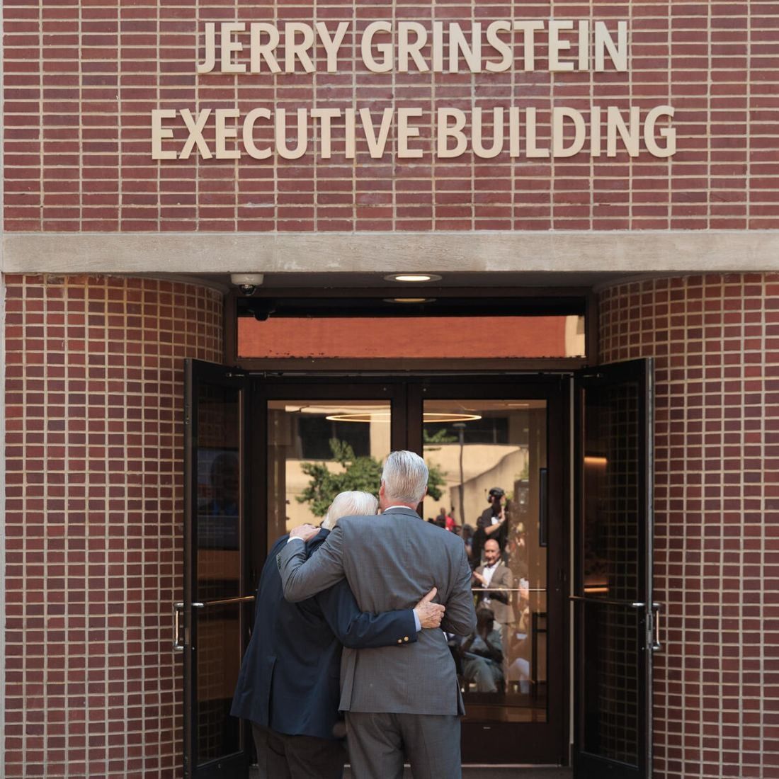 Delta Air Lines: Brick entrance with glass double doors under lettering reading Jerry Grinstein Executive Building, two men seen from behind