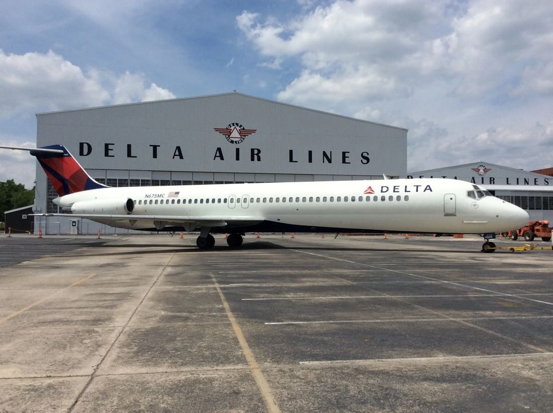 Large arched hangar with Delta Air Lines lettering and a jet parked on the apron in front