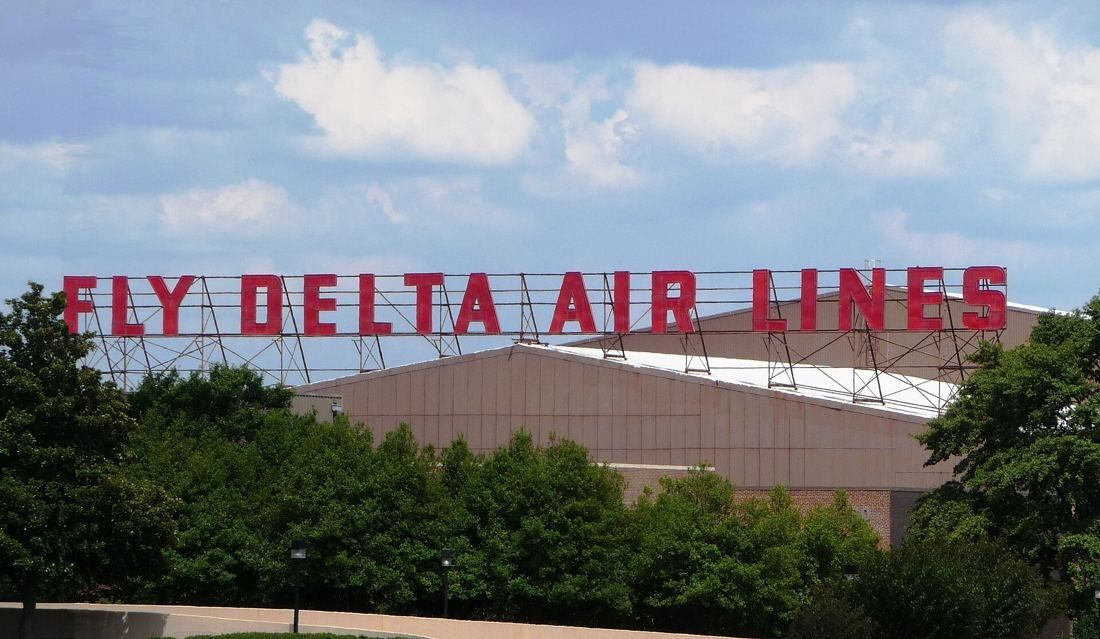 Delta Air Lines: Large red letters reading Fly Delta Air Lines standing on top of a low building behind trees