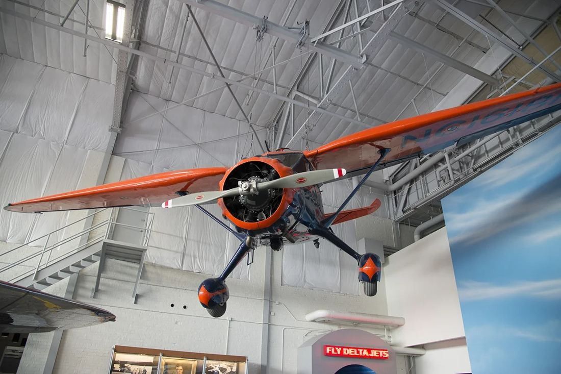 Delta Air Lines: Orange and silver single-engine vintage plane suspended from the roof structure of a hangar