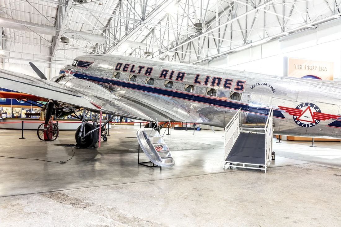 Delta Air Lines: Polished silver twin-engine propeller airliner with Delta Air Lines lettering parked inside a bright hangar with a steel roof truss