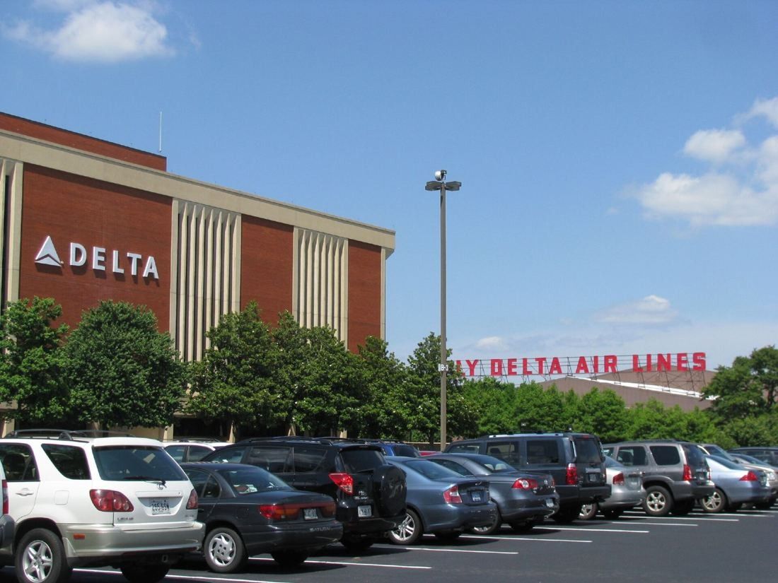 Delta Air Lines: Red-brick building with a Delta logo above a parking lot, with large red Fly Delta Air Lines letters in the distance