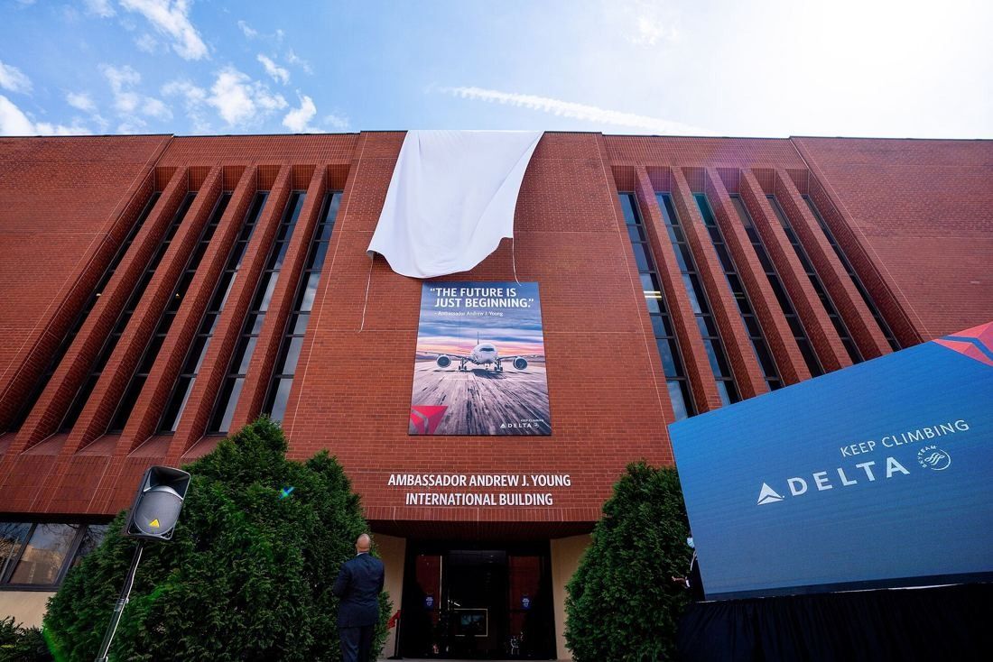 Delta Air Lines: Red-brick facade with tall vertical window slots, a large airplane banner and lettering reading Ambassador Andrew J. Young International Building