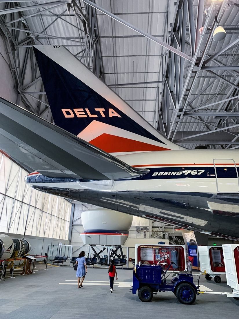 Delta Air Lines: Tall hangar interior with the nose and fuselage of a Boeing 767 in Delta livery and a small service vehicle on the floor