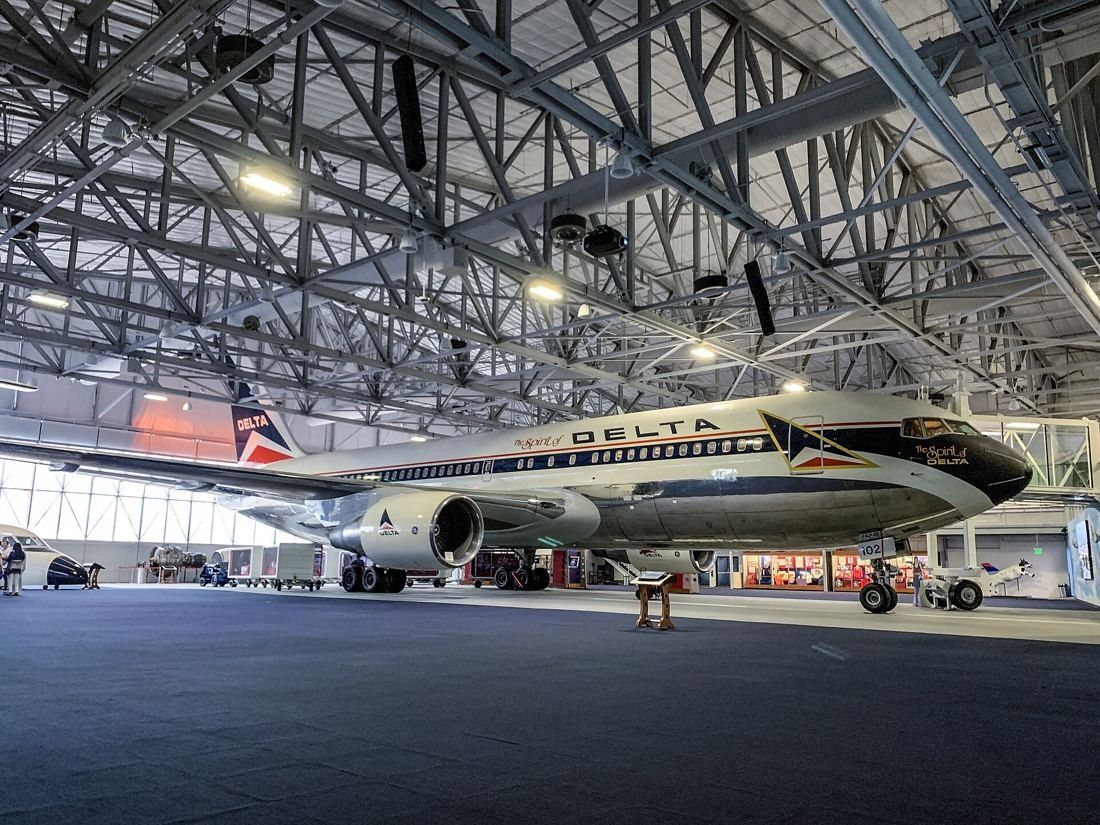 Delta Air Lines: Wide view of a hangar interior with exposed steel roof trusses and a Delta jet airliner on display