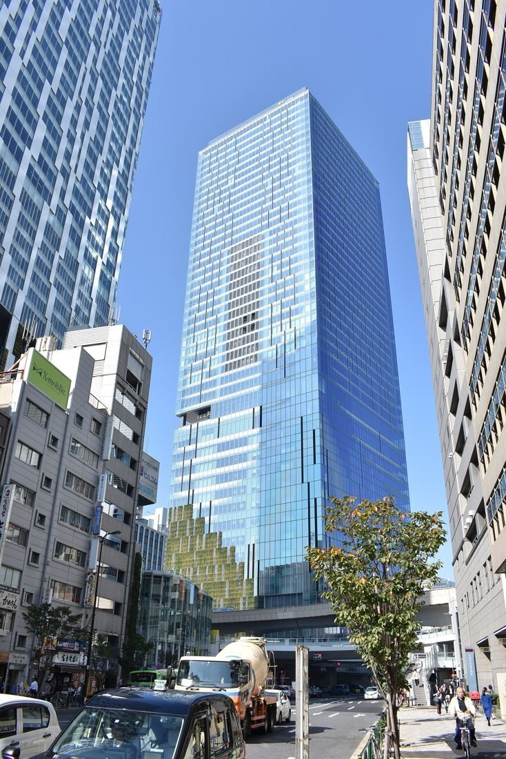 DeNA: Glass tower at the end of a street with trees and smaller buildings