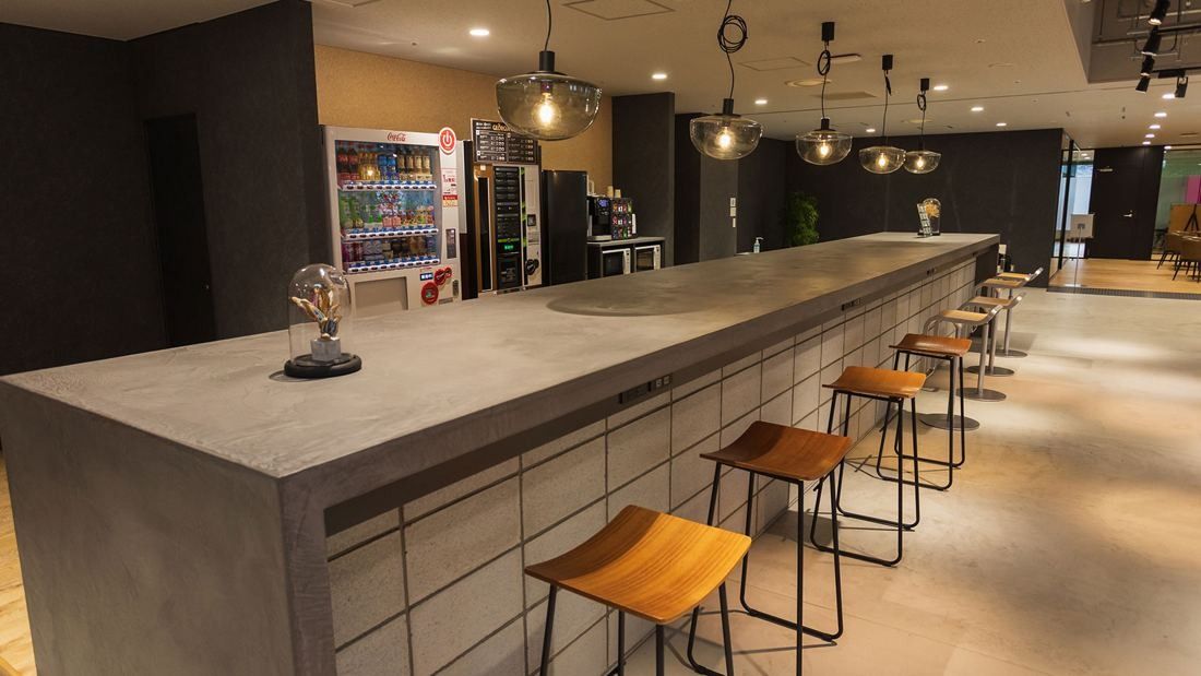 DeNA: Long concrete counter with wooden stools and pendant lights