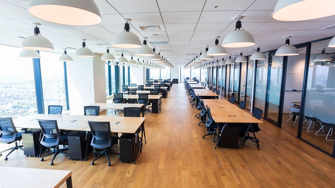 DeNA: Long office floor with rows of desks, pendant lamps and city views