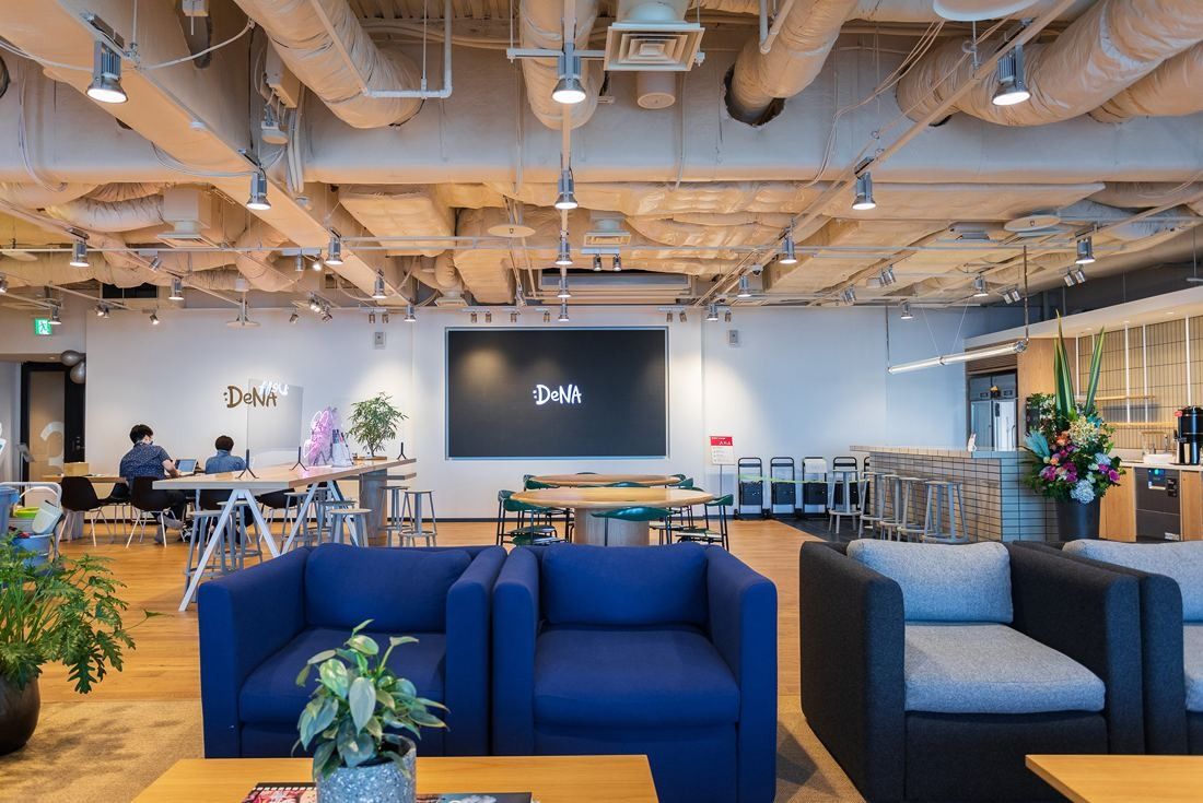 DeNA: Lounge with blue armchairs, a large wall screen with the DeNA logo and a counter