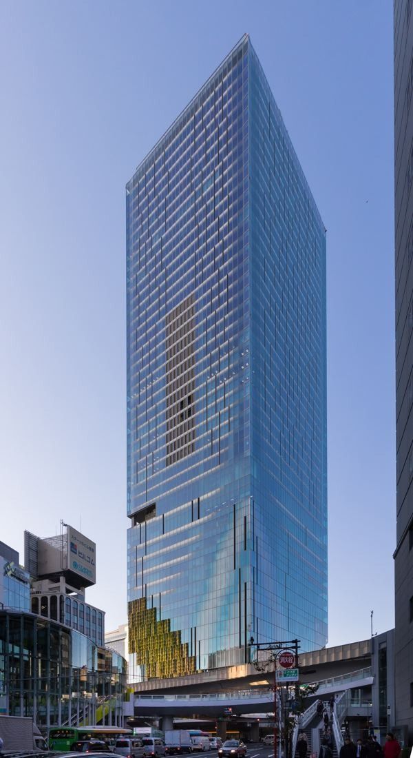 DeNA: Slender glass skyscraper seen from below against a blue sky
