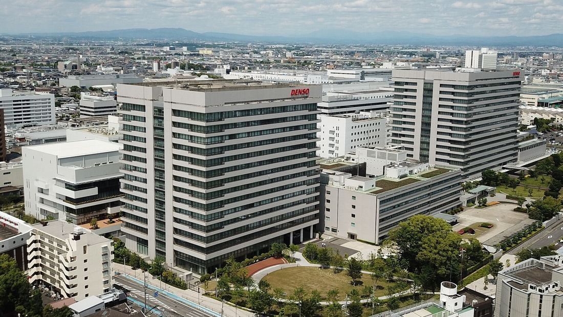 Aerial view of a campus of white high-rise office buildings with a round green park in the middle and a city stretching to the hills