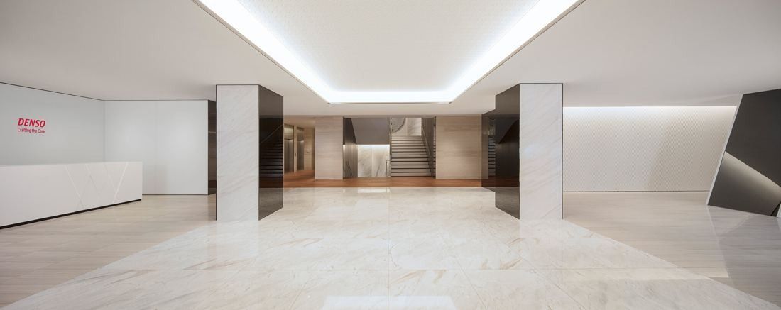 Denso: Bright entrance hall with pale marble floor, white columns, a white reception counter and a staircase at the back
