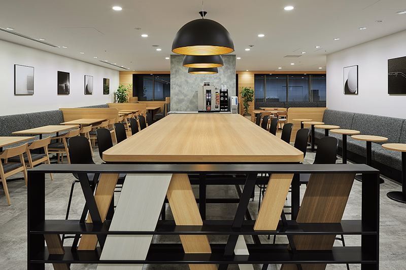 Denso: Café space with a long wooden table, black pendant lamps and upholstered booth seating