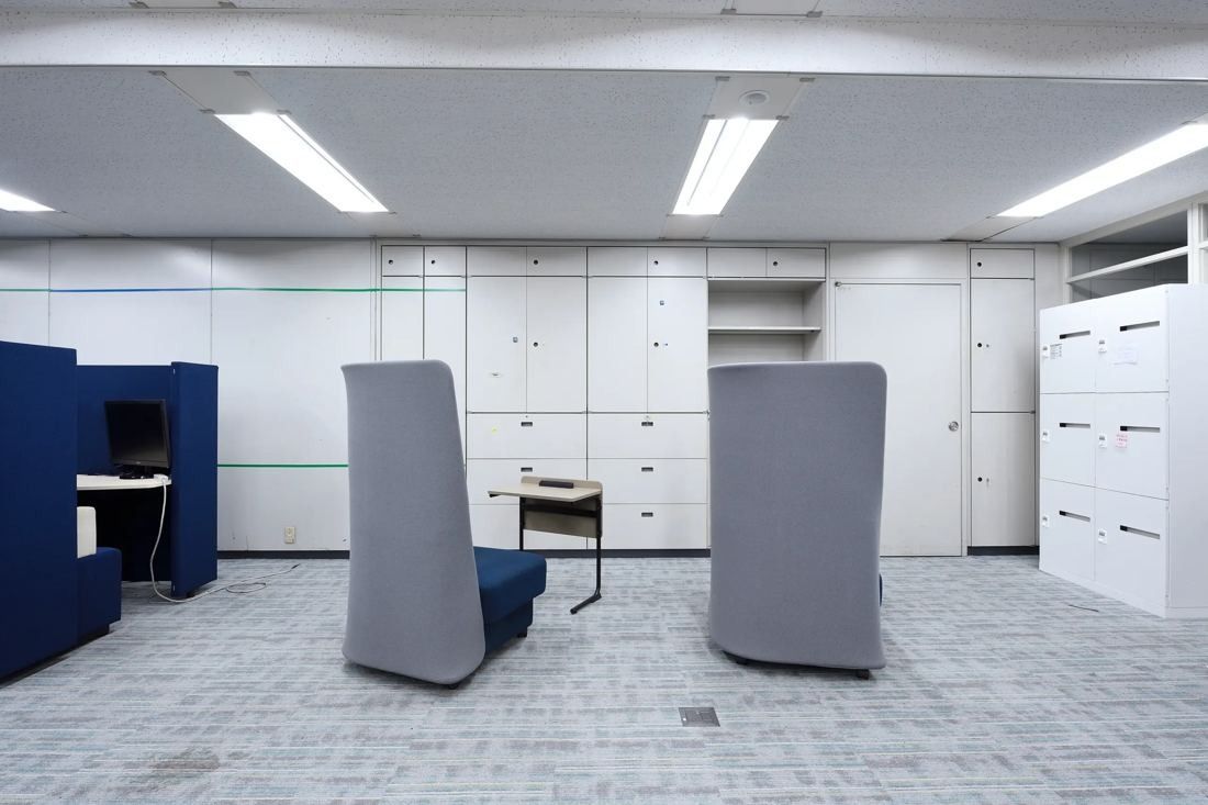Denso: Corner of an office with two grey high-backed lounge chairs, a navy booth and white lockers