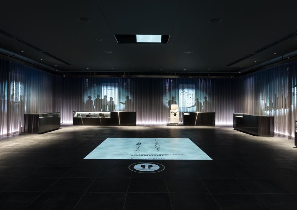 Denso: Dark exhibition hall with a glowing floor display in the centre and tall fabric screens around the walls