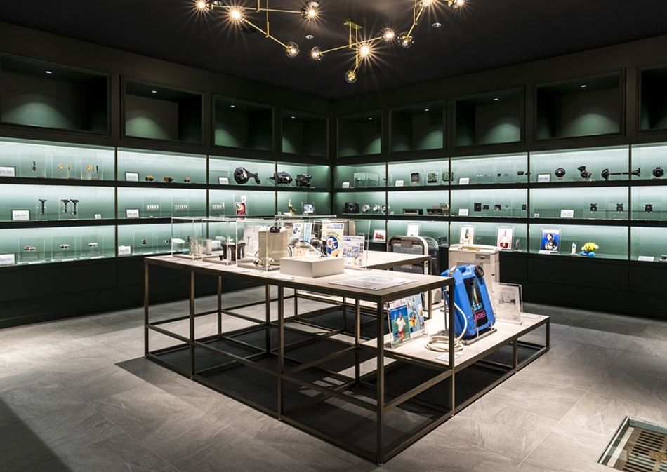 Denso: Dark exhibition room with glass shelves of small parts lining the walls around a central display table