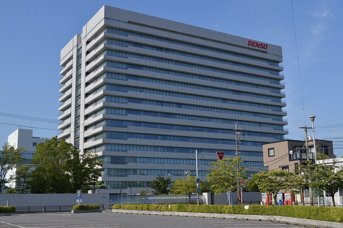 Denso: Tall white office tower with horizontal bands under a blue sky, trees and a low wall in front