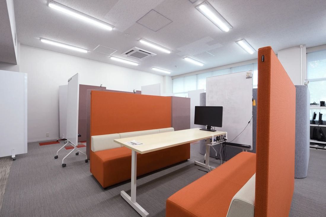 Denso: Work area with an orange high-backed booth, a white desk with a monitor and whiteboard panels