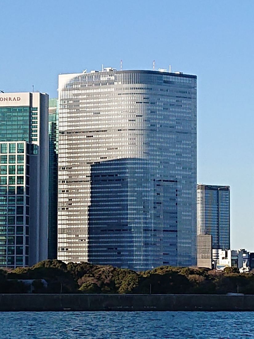Dentsu: A curved white-striped glass tower beside other high-rises across the water