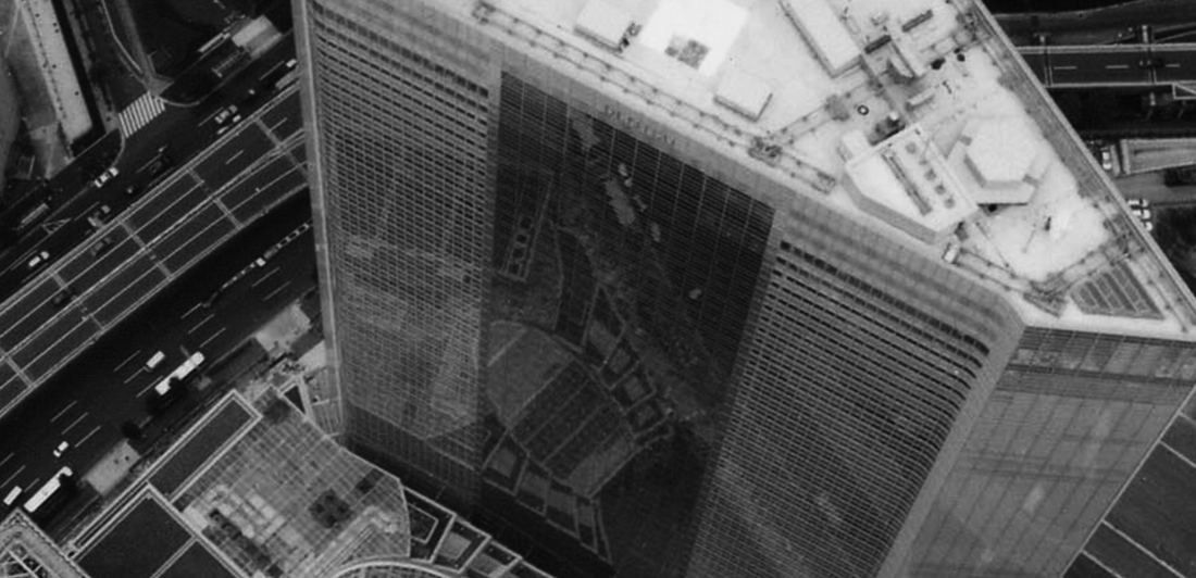 Dentsu: Black-and-white aerial view looking down on the roof and facade of a tower beside wide roads