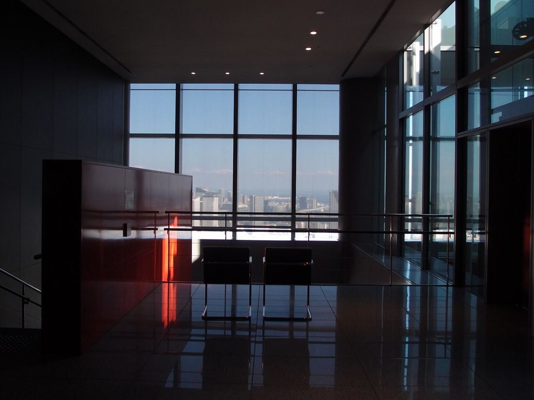 Dentsu: Dim upper-floor lobby with tall windows looking out over the city