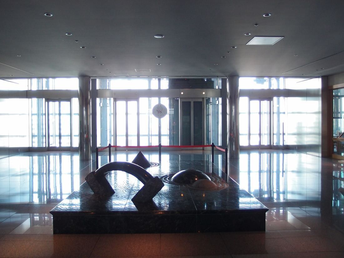 Dentsu: Elevator hall with a dark sculpture in front of tall glass doors