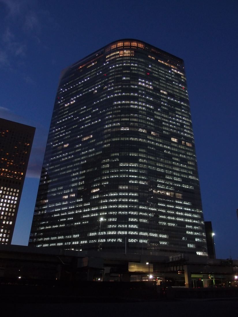 Dentsu: Glass tower glowing with lit office floors against a dark blue sky