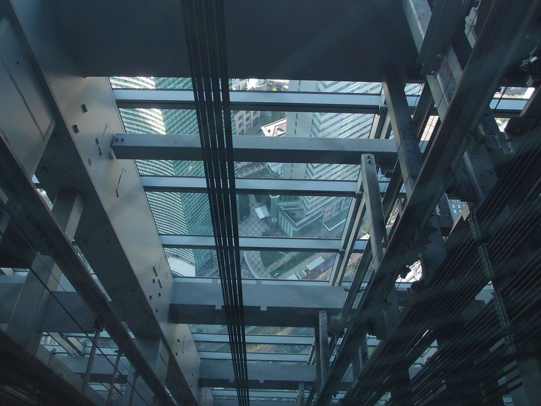 Dentsu: Looking down a glass elevator shaft with steel beams onto the streets far below
